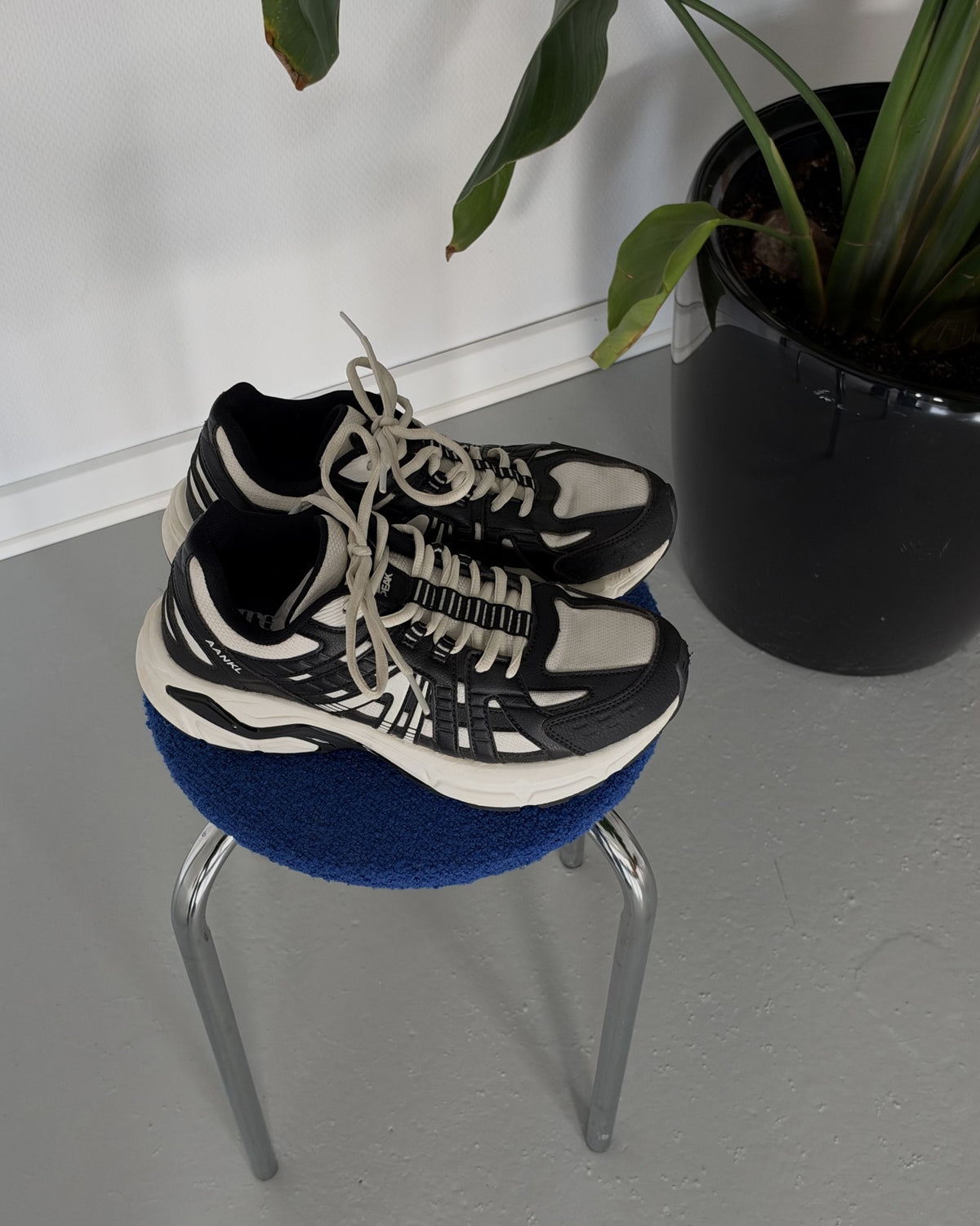 AANKL GLIDE Black/White – originalfoto af skoene på en blå skammel ved en plante