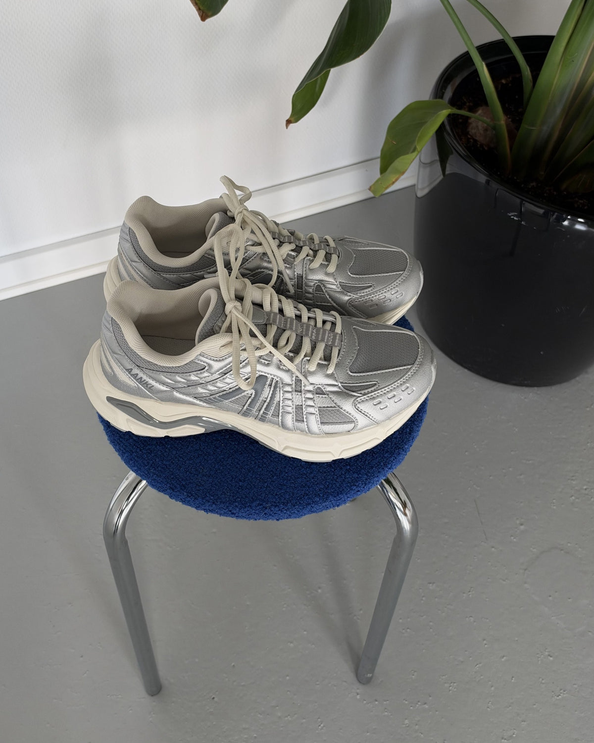 AANKL GLIDE Silver – originalfoto af skoene på en blå skammel ved en plante